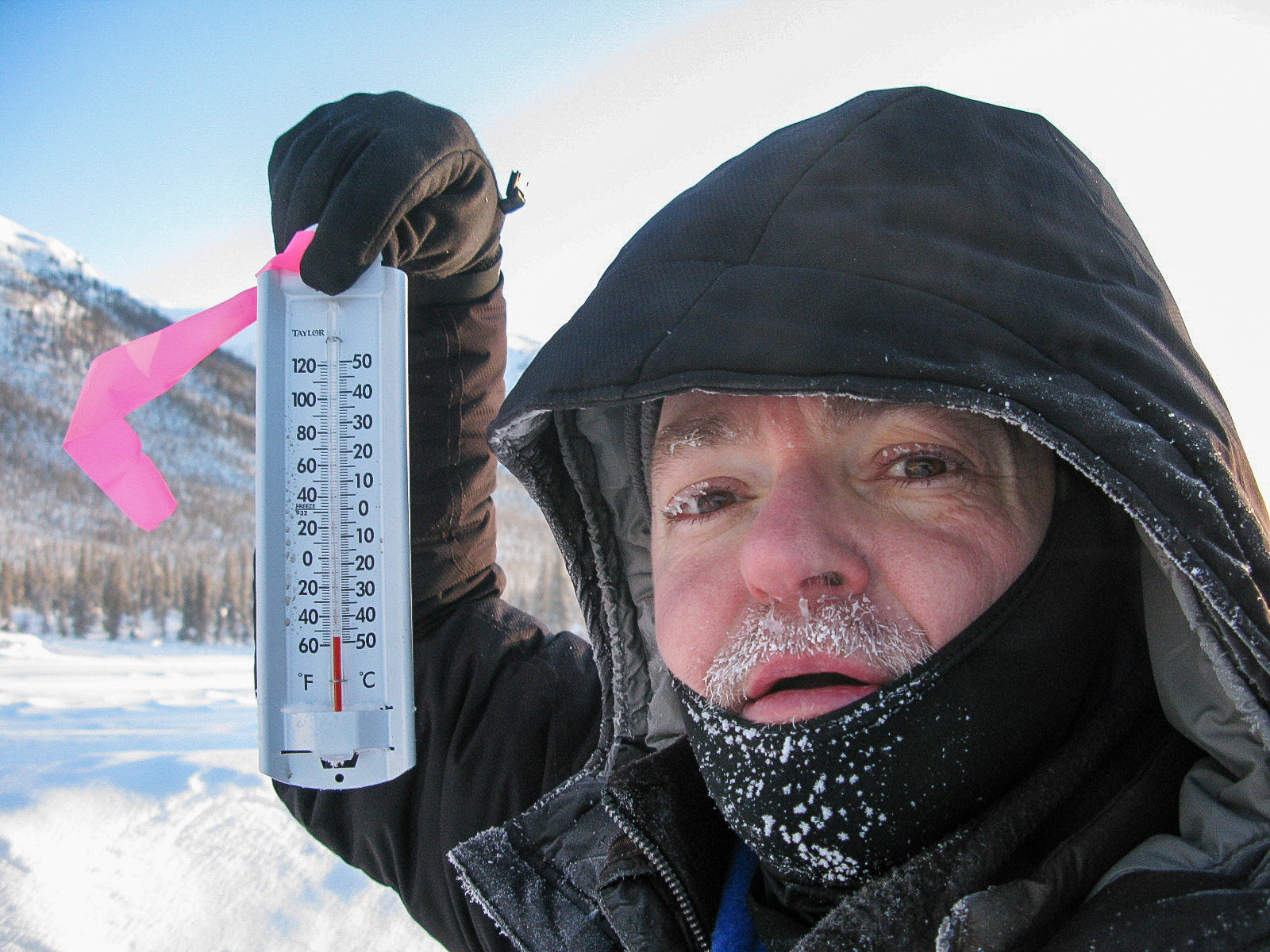 Person in extreme cold holding an outdoor thermometer reading far below zero