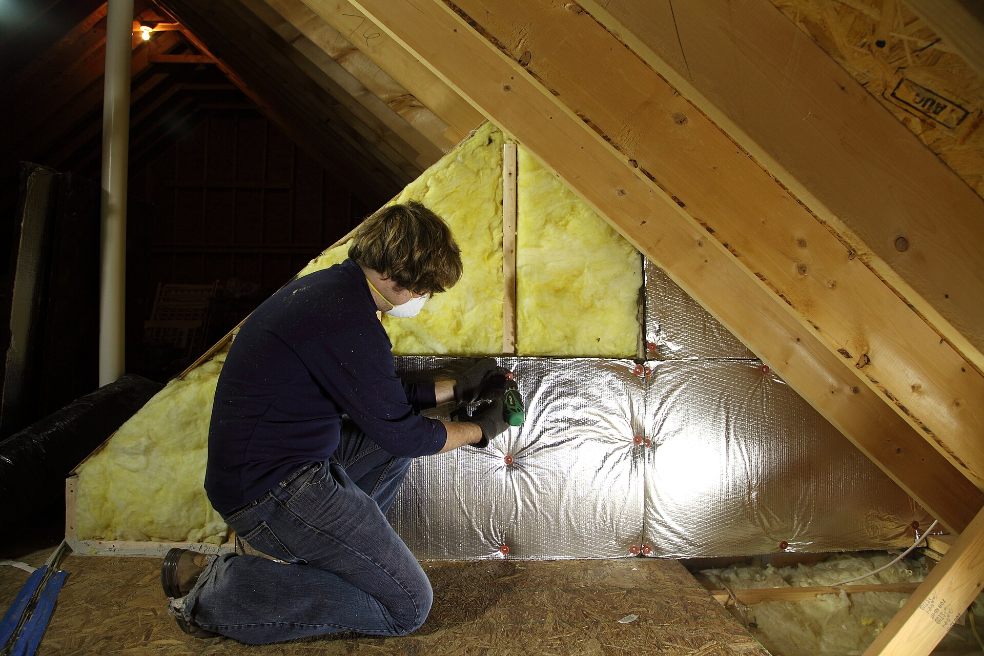 Installer placing fiberglass batt insulation between attic roof rafters