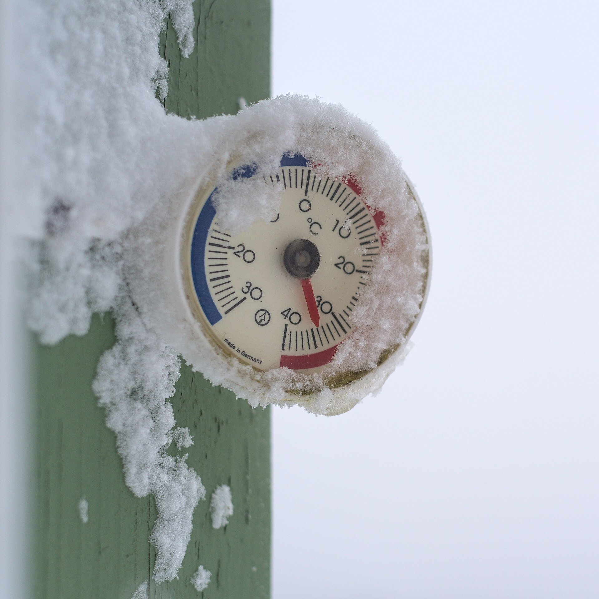 Outdoor thermometer iced over with frost on the dial and housing