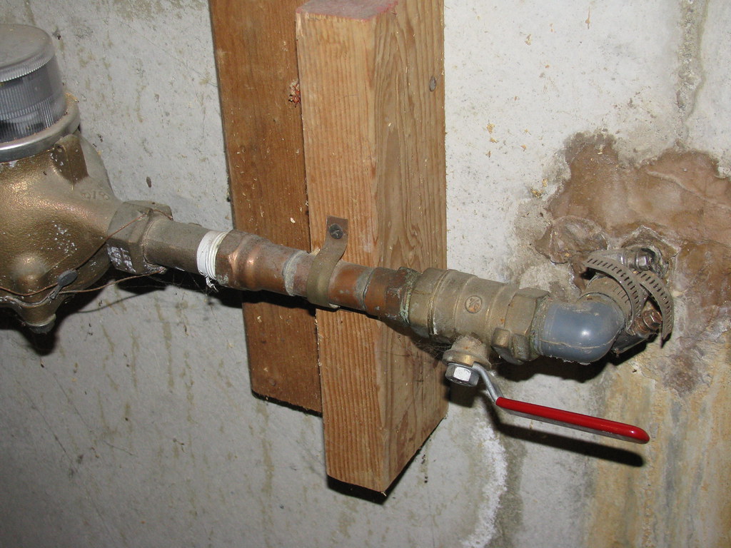 Copper water pipes, shut-off valve, and meter on a concrete utility wall